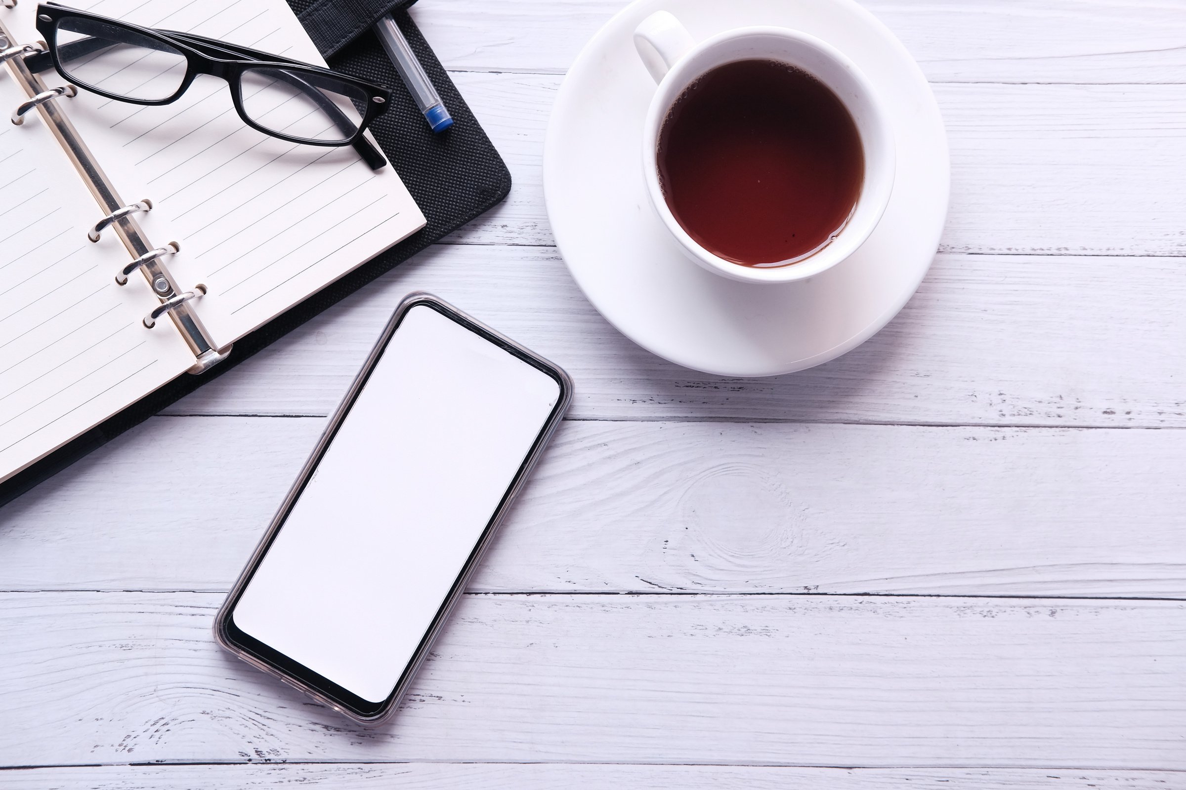 Smartphone, Coffee, Eyeglasses and a Notebook on a Wooden Background